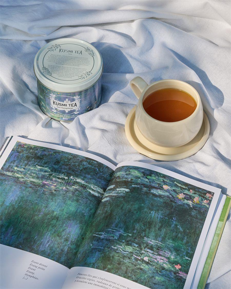 Tasse de thé vert Kusmi Tea à côté de la boîte Les Nymphéas et d'un livre ouvert sur les Nymphéas