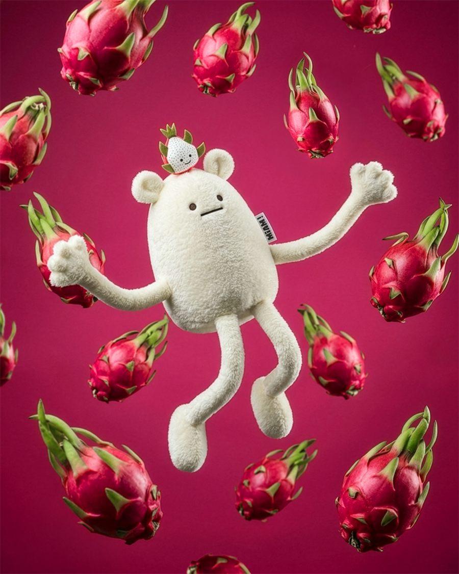 La peluche MIAM No Name, blanche, en lévitation parmi des fruits du dragon sur fond magenta