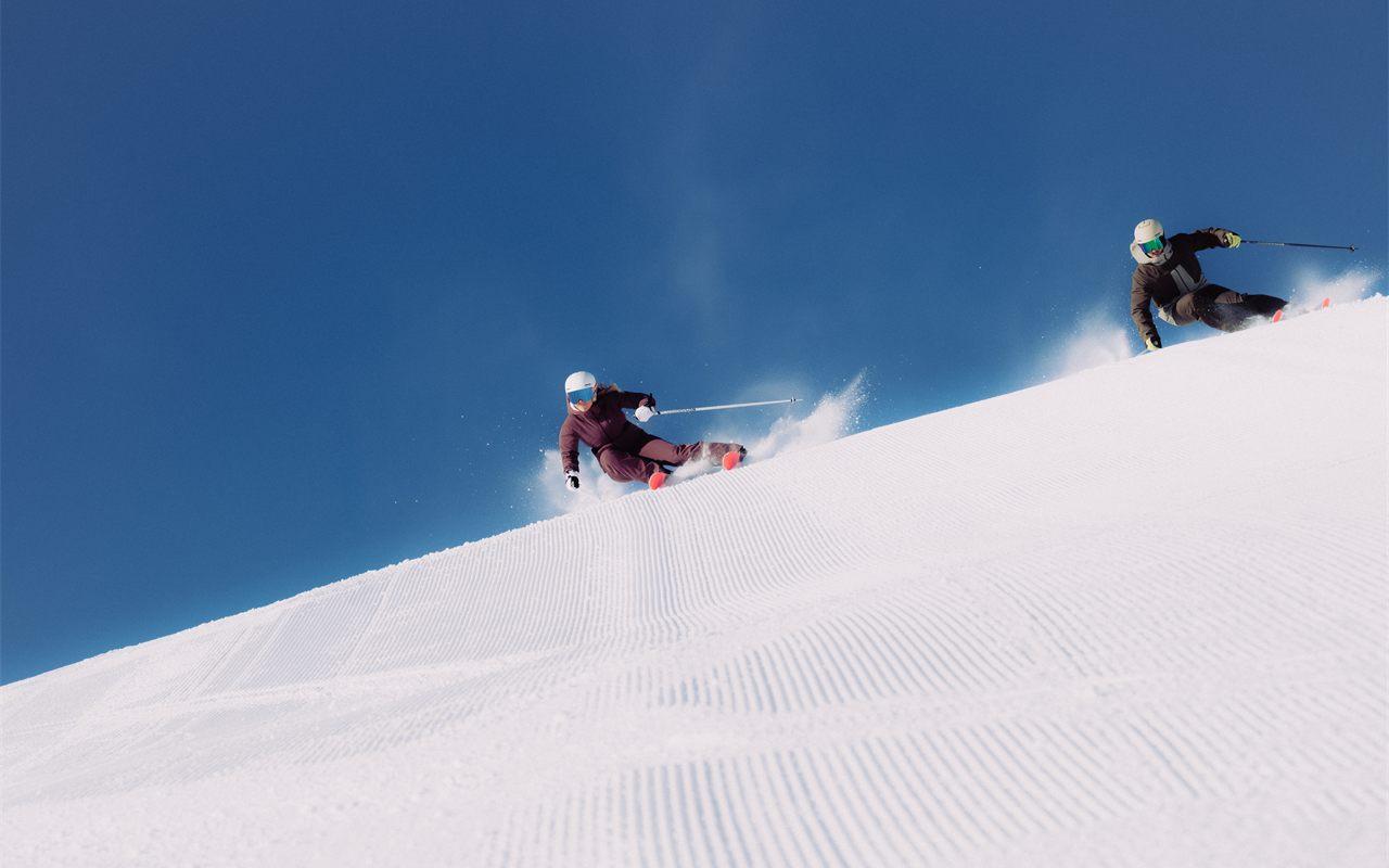 Deux skieurs en virage sur une piste damée, collection Rossignol Piste hiver 2026-2027