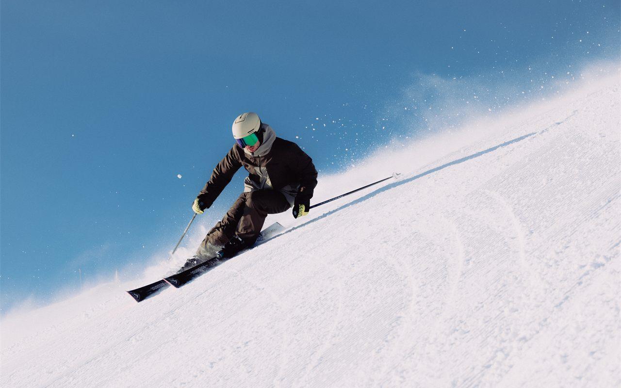 Skieur en courbe sur des skis Rossignol, soulevant la neige d'une piste damée